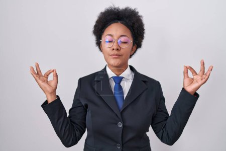 Photo for Beautiful african woman with curly hair wearing business jacket and glasses relaxed and smiling with eyes closed doing meditation gesture with fingers. yoga concept. - Royalty Free Image