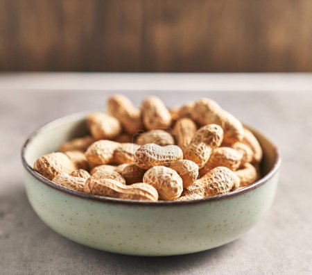Photo for A bowl full of unshelled peanuts on a wooden table, suggesting a natural, healthy snack. - Royalty Free Image