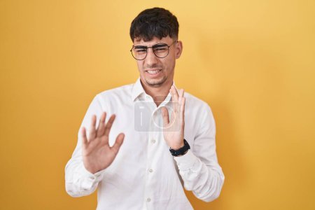 Téléchargez les photos : Young hispanic man standing over yellow background disgusted expression, displeased and fearful doing disgust face because aversion reaction. - en image libre de droit