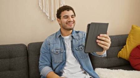 Ein lächelnder junger Mann mit Tablet genießt die Freizeit auf einem Sofa in gemütlicher Wohnzimmeratmosphäre.