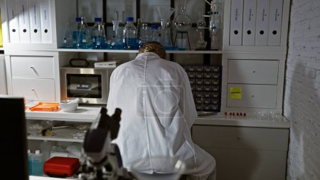 Foto de Vista posterior de una científica en una bata de laboratorio que examina la investigación en un entorno de laboratorio. - Imagen libre de derechos