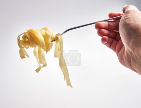 Téléchargez les photos : Gros plan d'une main tourbillonnant pâtes fettuccine sur une fourchette sur un fond blanc, représentant la cuisine italienne. - en image libre de droit