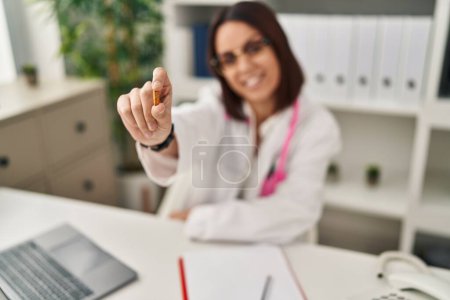 Téléchargez les photos : Young beautiful hispanic woman doctor smiling confident holding pill at clinic - en image libre de droit