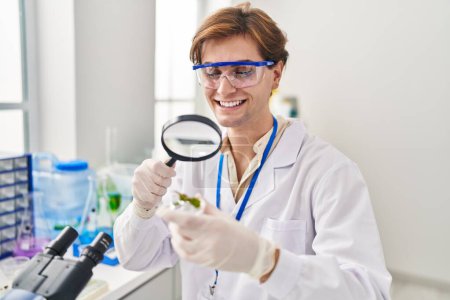 Téléchargez les photos : Young caucasian man scientist looking plant sample with loupe at laboratory - en image libre de droit