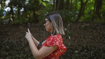 Foto de Sonriendo hermosa mujer hispana con gafas tomando una foto impresionante en el templo meiji, sumergiéndose en la cultura japonesa utilizando su tecnología de teléfonos inteligentes, disfrutar de la naturaleza en el parque verde tokyo. - Imagen libre de derechos