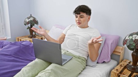 Foto de Joven hombre gestos, mientras que la videoconferencia en el ordenador portátil en acogedor dormitorio - Imagen libre de derechos