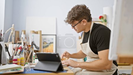 Photo for Attractive young hispanic man, a committed art student, fervently engrossed in drawing on his touchpad and notebook at his studio - Royalty Free Image