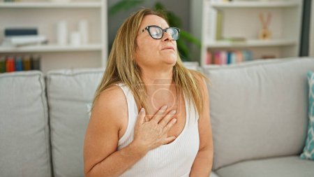 Photo for Middle age hispanic woman sitting on sofa suffering heart attack at home - Royalty Free Image