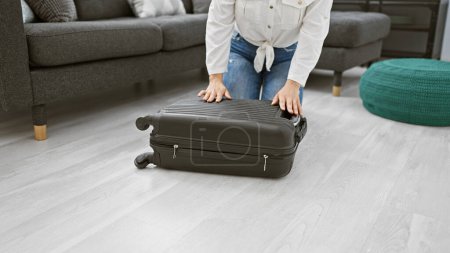 Téléchargez les photos : Jeune femme emballant une valise dans un salon rangé, prête pour le voyage. - en image libre de droit