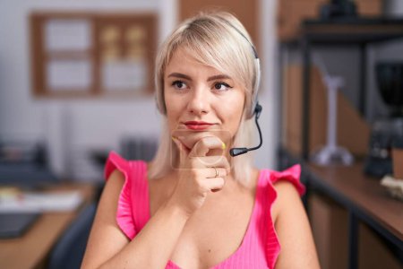 Photo for Young caucasian woman wearing call center agent headset serious face thinking about question with hand on chin, thoughtful about confusing idea - Royalty Free Image