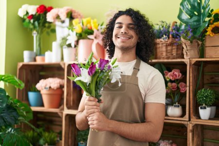 Téléchargez les photos : Jeune homme latin fleuriste tenant bouquet de fleurs à la boutique de fleurs - en image libre de droit