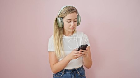 Young blonde woman listening to music over isolated pink background