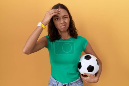 Photo for Young hispanic woman holding ball worried and stressed about a problem with hand on forehead, nervous and anxious for crisis - Royalty Free Image