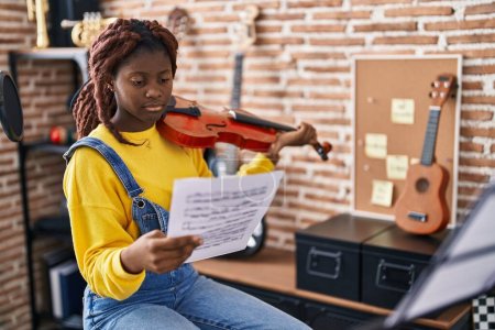 Photo for African american woman musician playing violin looking music sheet at music studio - Royalty Free Image