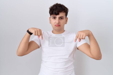 Photo for Young non binary man wearing casual white t shirt pointing down looking sad and upset, indicating direction with fingers, unhappy and depressed. - Royalty Free Image