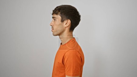 Photo for Attractive young hispanic man in deep concentration, standing relaxed, eyes looking away to the side against a stark, isolated white background wall. - Royalty Free Image
