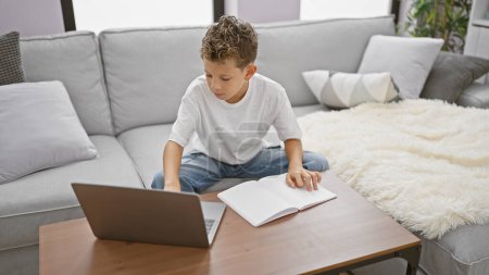 Photo for Adorable blond boy, a budding wordsmith, engrossed in putting pen to paper with his laptop's assistance, writing his ideas in a notebook, comfortably perched in his home's living room. - Royalty Free Image