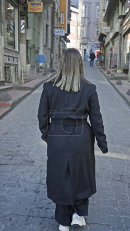Téléchargez les photos : Vue arrière d'une jeune femme marchant seule dans une rue historique d'Istanbul, dépeignant l'exploration urbaine. - en image libre de droit