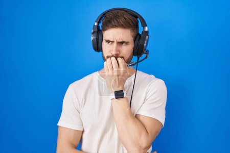 Photo for Hispanic man with beard listening to music wearing headphones looking stressed and nervous with hands on mouth biting nails. anxiety problem. - Royalty Free Image