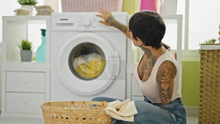 Foto de Mujer hispana con brazo amputado lavando ropa sentada en el suelo en la lavandería - Imagen libre de derechos