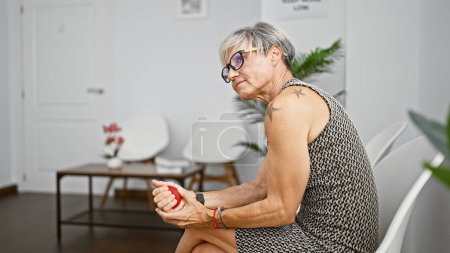 Photo for Mature hispanic woman with short grey hair squeezing a stress ball in an indoor waiting room. - Royalty Free Image