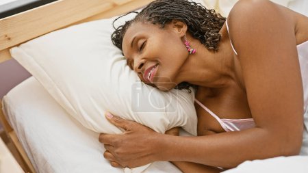 Téléchargez les photos : Femme afro-américaine se relaxant dans une chambre à coucher avec une expression joyeuse, reflétant loisirs et confort. - en image libre de droit