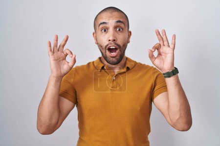 Téléchargez les photos : Hispanic man with beard standing over white background looking surprised and shocked doing ok approval symbol with fingers. crazy expression - en image libre de droit