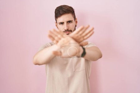 Foto de Hombre hispano con barba de pie sobre fondo rosa expresión de rechazo cruzando brazos y palmas haciendo signo negativo, cara enojada - Imagen libre de derechos