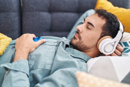 Téléchargez les photos : Jeune homme hispanique écoutant de la musique dormir sur le canapé à la maison - en image libre de droit