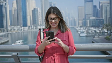 Foto de Mujer sonriente usando teléfono inteligente con el horizonte del puerto deportivo de Dubái en segundo plano - Imagen libre de derechos