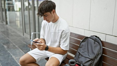 Téléchargez les photos : Jeune adolescent hispanique étudiant utilisant un smartphone assis sur un banc à l'université - en image libre de droit