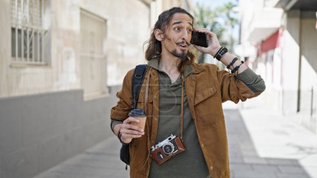 Foto de Joven turista hispano hablando en smartphone sosteniendo café en la calle - Imagen libre de derechos