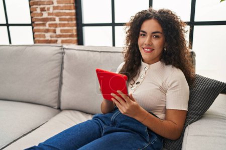 Téléchargez les photos : Jeune belle femme hispanique utilisant touchpad assis sur le canapé à la maison - en image libre de droit