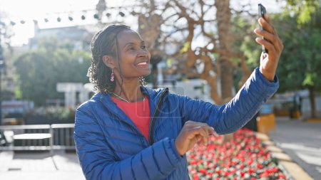 Téléchargez les photos : Femme afro-américaine prenant un selfie dans un cadre extérieur urbain ensoleillé - en image libre de droit