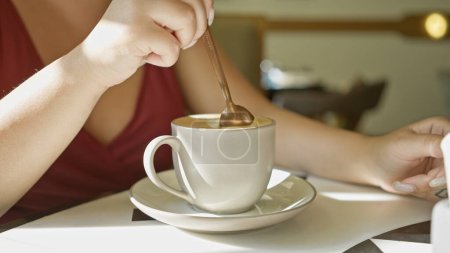 Foto de Una mujer adulta joven agita el café en un café brillante, mostrando una experiencia de comedor interior informal. - Imagen libre de derechos