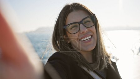 Photo for A happy young woman in eyeglasses enjoys a sunny day by the sea with clear skies in the background. - Royalty Free Image
