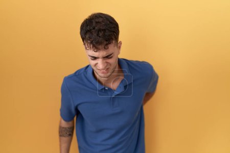 Photo for Young hispanic man standing over yellow background suffering of backache, touching back with hand, muscular pain - Royalty Free Image