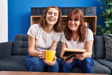 Téléchargez les photos : Two women mother and daughter drinking coffee looking photo at home - en image libre de droit