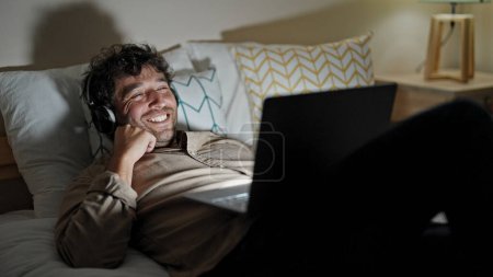 Téléchargez les photos : Jeune homme hispanique regardant un film allongé sur le lit dans la chambre - en image libre de droit
