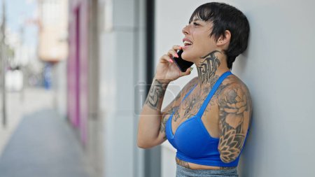 Téléchargez les photos : Femme hispanique avec le bras amputé souriant confiant parler sur le smartphone à la rue - en image libre de droit