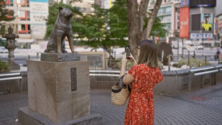 Téléchargez les photos : Belle femme hispanique à lunettes prenant des photos mémorables à la statue de hachiko dans le paysage urbain de tokyo - en image libre de droit
