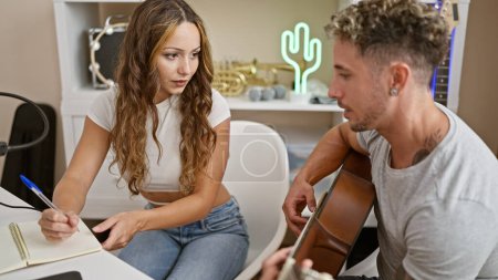 A man and a woman collaborate musically in a studio, with a guitar and notebook, focused on songwriting.