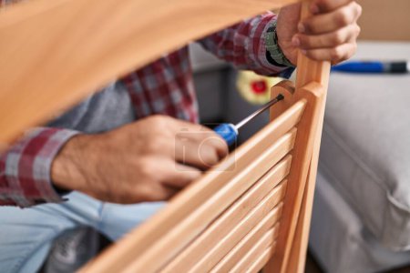 Photo for Young hispanic man repairing chair at new home - Royalty Free Image
