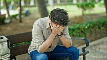 Foto de Joven hispano estresado sentado en el banco del parque - Imagen libre de derechos