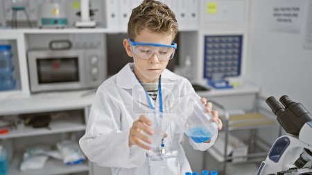 Foto de Adorable científico niño rubio seriamente comprometido en un experimento químico, vertiendo líquido en el tubo de ensayo mientras trabajaba en el laboratorio - Imagen libre de derechos