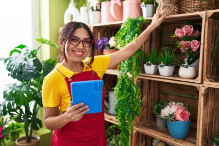 Téléchargez les photos : Jeune belle fleuriste arabe femme en utilisant touchpad tenant plante de rayonnage à la boutique de fleurs - en image libre de droit