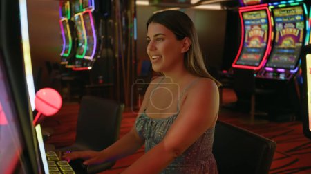 Téléchargez les photos : Jeune femme hispanique jouant machine à sous, exsudant la joie dans un casino animé - en image libre de droit