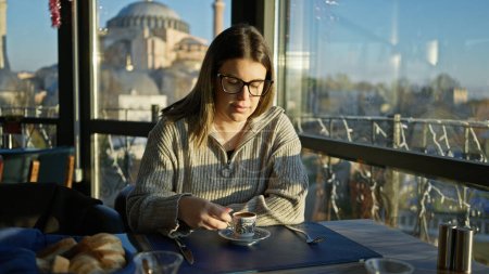 A young woman enjoys coffee in a turkish restaurant with a view of istanbul's hagia sophia.