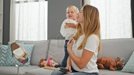 Téléchargez les photos : Mère caucasienne confiante s'assoit confortablement, peigner les cheveux de sa fille sur le canapé - scène de famille chaleureuse à la maison - en image libre de droit