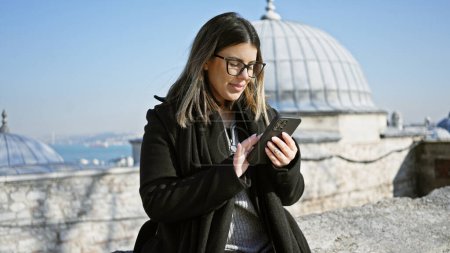 Téléchargez les photos : Femme hispanique adulte utilisant un smartphone avec un paysage urbain istanbul en arrière-plan. - en image libre de droit